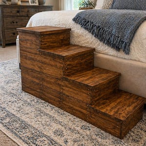 May include: A wooden pet step stool with four steps. The steps are stained a warm brown and are constructed with visible nail heads. The step stool is placed on a patterned rug in a bedroom setting.