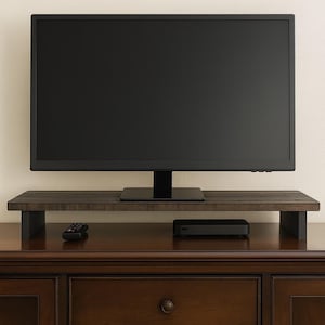 May include: A dark brown wooden TV stand with a black flat-screen television on top. A remote and a black media device are on the stand. The stand is on top of a dark brown wooden cabinet.