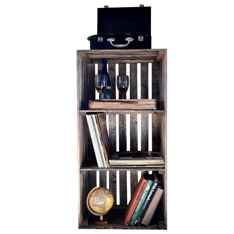 May include: A three-tier wooden crate shelf with a black suitcase on top, two wine glasses, a bottle of wine, a stack of vinyl records, a globe, and several books. The crate shelf is made of reclaimed wood and has a rustic look.