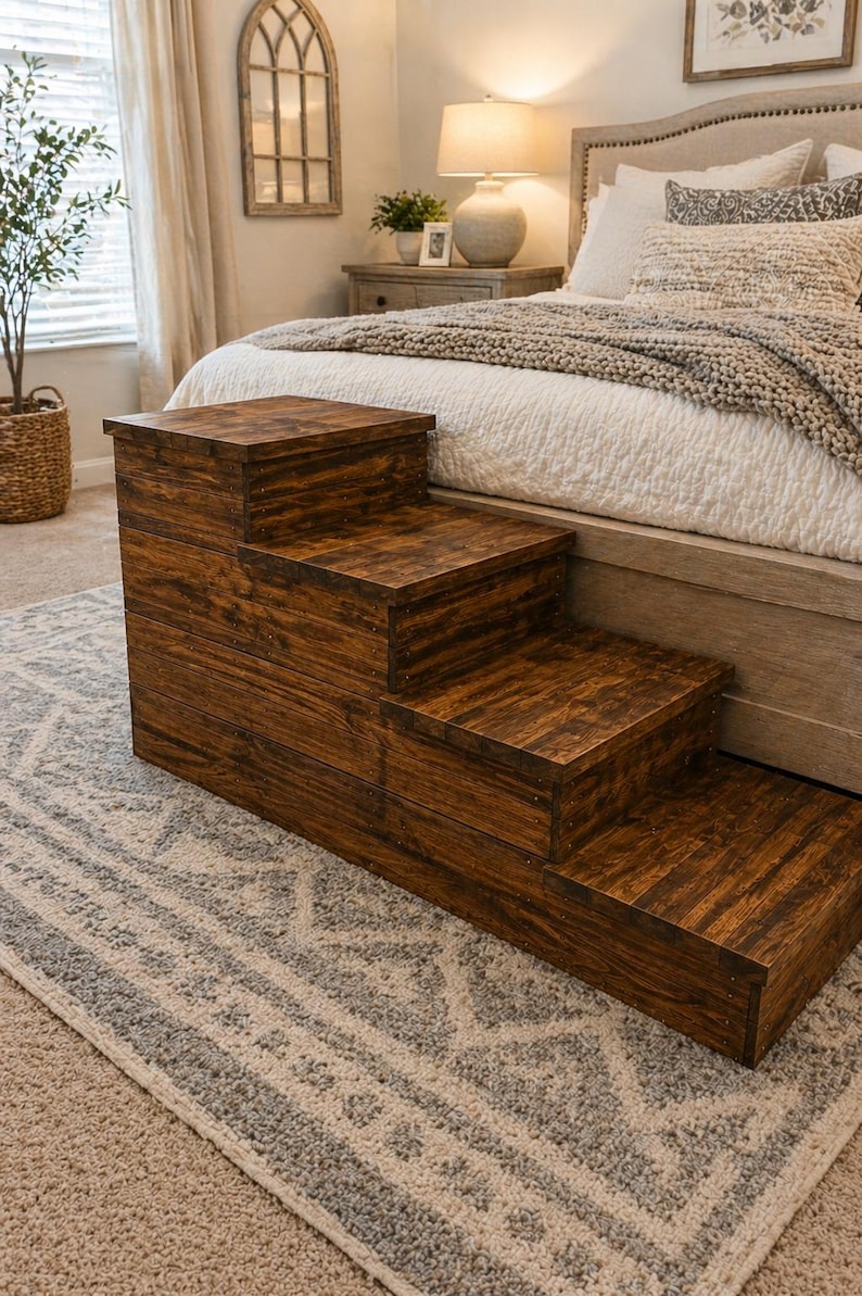 May include: A wooden pet step stool with three steps, stained in a dark brown color. The steps are rectangular and the wood grain is visible. The step stool is placed in front of a bed.
