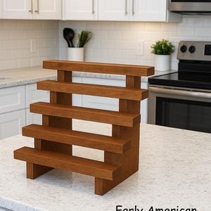 May include: A wooden, tiered spice rack with five shelves. The rack is made of a warm, medium-toned wood and is labeled "Early American". The shelves are supported by vertical beams, creating a stepped design. It is displayed on a white countertop.
