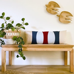 May include: A wooden bench with a white and red striped pillow. The pillow has a navy blue stripe on each end. Two wooden bird sculptures are on the wall behind the bench.
