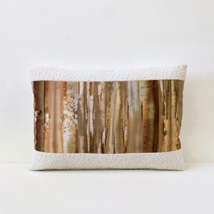 May include: Rectangular decorative pillow with a textured white border and a central panel featuring vertical streaks of brown, gold, and white. The pillow has a soft, inviting appearance, suitable for home decor.