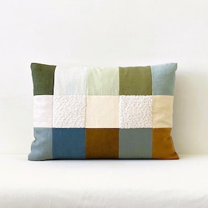 May include: A rectangular patchwork pillow with a variety of colors and textures, including green, blue, brown, white, and cream.
