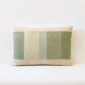 May include: Rectangular decorative pillow with a patchwork design. The pillow features a light beige border and a central panel with vertical stripes in shades of green and beige. The pillow is designed for home decor.