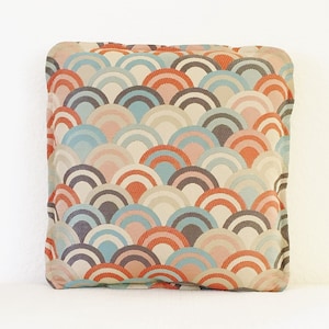 May include: A decorative pillow with a geometric pattern of overlapping, colorful arches in shades of peach, blue, gray, and brown.