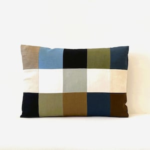 Peut inclure: Un coussin rectangulaire avec un motif patchwork. Le coussin est composé de neuf carrés de couleurs et de tissus différents, dont le beige, le bleu, le noir, le vert, le blanc et le marron.