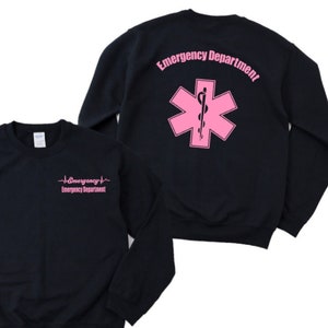 May include: Black sweatshirt with a pink "Emergency Department" text and a pink star of life symbol on the back. The front of the sweatshirt has a pink "Emergency Department" text with a heartbeat symbol.