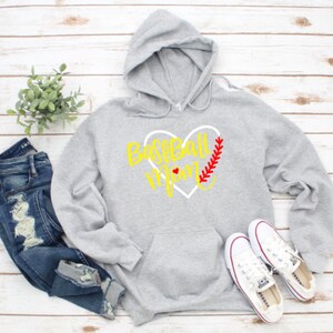 May include: Grey hooded sweatshirt with a white heart design and the text "Baseball Mom" in yellow. The heart has a red baseball stitch design.