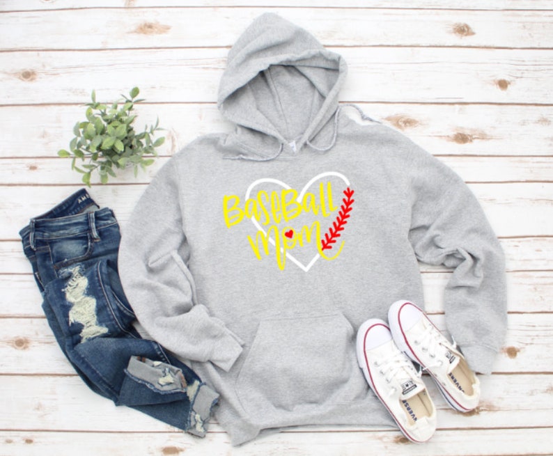 May include: Grey hooded sweatshirt with a white heart design and the text "Baseball Mom" in yellow. The heart has a red baseball stitch design.