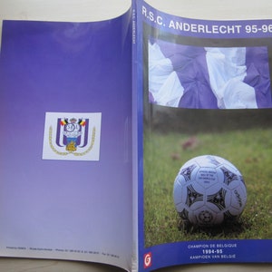 Puede incluir: Un programa vintage del R.S.C. Anderlecht 95-96. La portada presenta un balón de fútbol sobre hierba, el logo del equipo y texto en inglés y holandés. Un artículo de colección.