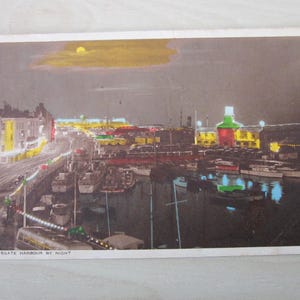 Puede incluir: Postal vintage que representa el puerto de Ramsgate por la noche. La imagen muestra un puerto lleno de barcos, iluminado por luces de colores de edificios y farolas. Una luna amarilla es visible en el cielo nocturno. El texto "RAMSGATE HARBOUR BY NIGHT" está impreso en la parte inferior.