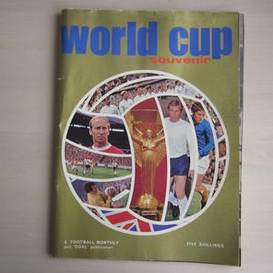 Peut inclure: Une couverture de magazine verte et dorée avec le texte "World Cup Souvenir" et un collage de photos de joueurs de football et d'un ballon de football.