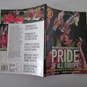 Könnte beinhalten: Ein Buch mit dem Titel "Manchester United Pride of All Europe" mit einem roten und weißen Cover, das ein Foto eines Fußballspielers zeigt, der eine Trophäe hochhält. Das Buch handelt von der Champions-League-Saison 1998/99 und enthält ein Vorwort von Alex Ferguson.