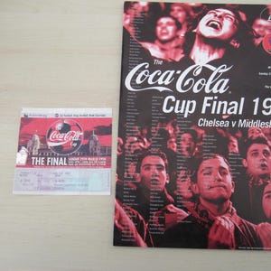 Könnte beinhalten: Ein Programm und eine Eintrittskarte für das Coca-Cola Cup Final 1998. Das Programm ist schwarz mit roten Akzenten und zeigt eine Menschenmenge. Die Eintrittskarte ist rot und weiß mit dem Coca-Cola-Logo und der Aufschrift "THE FINAL".