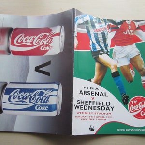 May include: A Coca-Cola Cup final matchday program featuring Arsenal vs Sheffield Wednesday. The program cover features a photo of two soccer players in action, one in a red and white jersey and the other in a blue and white jersey. The program cover also features the Coca-Cola Cup logo and the date of the match, Sunday 1st April 1993.