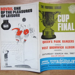 May include: Open vintage football program featuring a cartoon illustration of a soccer match and the text "Bovril One of the Pleasures of Leisure." The right side displays "Cup Final" and details of the Queen's Park Rangers versus West Bromwich Albion game.