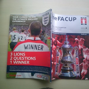 May include: A red and white program for the FA Cup Final between Arsenal and Southampton on May 17, 2003. The cover features the FA Cup trophy and players from both teams. The back of the program has a contest to win an England experience.