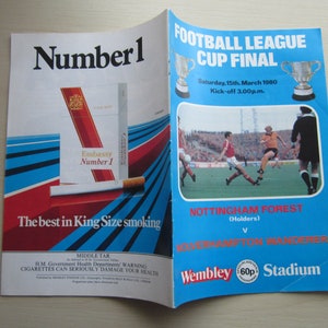 May include: A blue and white programme for the Football League Cup Final held on Saturday, 15th March 1980 at Wembley Stadium. The game was between Nottingham Forest (Holders) and Wolverhampton Wanderers. The programme features a photo of the game and an advertisement for Embassy Number 1 cigarettes.