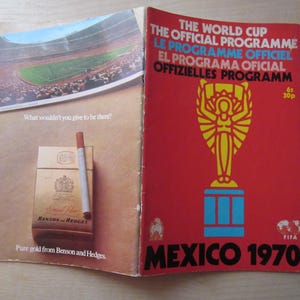 May include: A red, white, and blue program for the 1970 FIFA World Cup in Mexico. The cover features the World Cup trophy and the text "THE WORLD CUP THE OFFICIAL PROGRAMME LE PROGRAMME OFFICIEL EL PROGRAMA OFICIAL OFFIZIELLES PROGRAMM 61 30p FIFA MEXICO 1970".