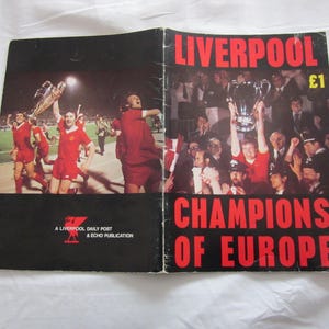 Könnte beinhalten: Ein Vintage-Magazin des FC Liverpool. Auf dem Cover stehen in Rot "LIVERPOOL" und "CHAMPIONS OF EUROPE". Innen zeigen Bilder die Mannschaft beim Feiern mit der Trophäe.