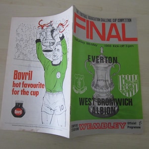 May include: A vintage football program from the 1968 Football Association Challenge Cup Final. The cover is green and white, featuring the teams Everton and West Bromwich Albion. The program also includes a cartoon illustration of a player holding a trophy.