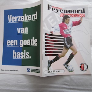 May include: An open magazine spread featuring a soccer player in a red and white Feyenoord uniform kicking a soccer ball. Text includes "Feyenoord Jeugdtoernooi" and "Nr.1 22 mei". The left page has Dutch text.