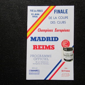 May include: A vintage event program for the 1956 European Cup Final between Madrid and Reims, held at Parc des Princes on June 13th. The program features text in French, with a red, yellow, and blue color scheme and a champagne advertisement.