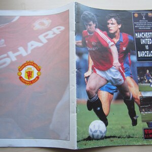 May include: A vintage Manchester United vs. Barcelona match program. The cover features players in red and blue uniforms, with the text "MANCHESTER UNITED VS BARCELONA." The Manchester United logo is visible.
