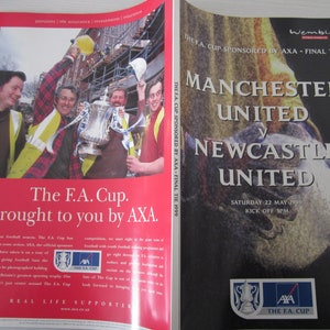May include: A magazine spread featuring a red page with the text "The F.A. Cup. Brought to you by AXA." and a photo of people celebrating with a trophy. The opposite page has a poster for the Manchester United vs. Newcastle United match.