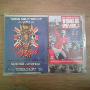 May include: Two encased items featuring the 1966 World Cup Final. One is a blue poster with the text "World Championship Jules Rimet Cup Final England v West Germany." The other is a DVD case with the text "The World Cup Final 1966 England v West Germany."