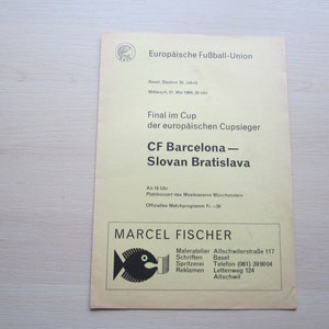 May include: A yellow and black printed flyer for the European Cup Final between CF Barcelona and Slovan Bratislava. The game will be held on May 21, 1968 at 8:00 PM in Basel, Switzerland at the St. Jakob Stadium. The flyer also includes the text "Final im Cup der europäischen Cupsieger" and "Ab 19 Uhr Platzkonzert des Musikvereins Münchenstein Offizielles Matchprogramm Fr.-.50".