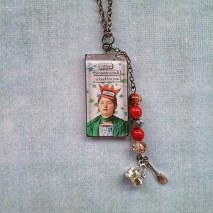 May include: A silver chain necklace with a rectangular glass pendant featuring a woman with a crown and the text "Coffee Because crack is bad for you". The pendant is surrounded by red, orange, and clear glass beads. The necklace also has a silver charm of a coffee cup and spoon.