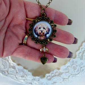 May include: A bronze pendant necklace with a round glass cameo featuring a brown and white dog. The cameo is surrounded by a decorative bronze frame. The necklace has a heart charm with the word "love" on it and a strand of crystal beads.