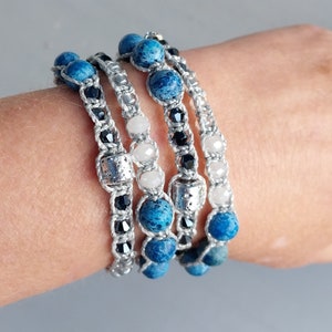 May include: Four bracelets with blue and white beads, black beads, and silver beads. The bracelets are layered on a person's wrist.