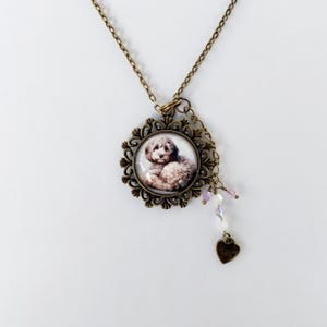 May include: A bronze necklace with a round pendant featuring a white dog. The pendant has a decorative filigree frame and is accented with a small heart charm and a strand of iridescent beads.