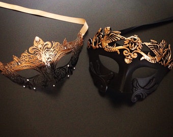 Può includere: Due maschere da maschera, una nera con accenti dorati e una dorata con accenti neri. Entrambe le maschere hanno disegni intricati e sono perfette per un ballo in maschera o una festa in costume.