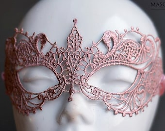 May include: A rose gold lace masquerade mask with delicate floral patterns. The mask is worn on a white mannequin head.