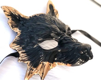 Puede incluir: Una máscara de lobo negra con detalles dorados. La máscara tiene un diseño detallado y está hecha de un material duro.