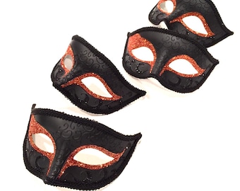 May include: Four black masquerade masks with orange glitter accents. The masks have a traditional Venetian design with intricate details.