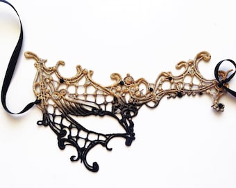 May include: A black and gold lace masquerade mask with rhinestones. The mask has a delicate, intricate design and is tied with a black ribbon.