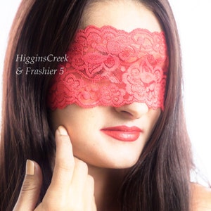 May include: A woman with long dark hair is wearing a red lace eye mask. Her lips are painted a bright red.