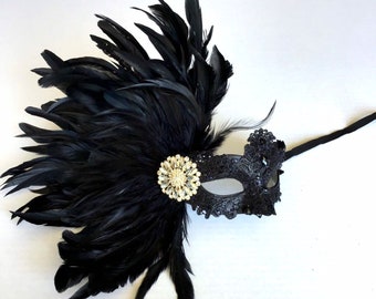 May include: Black masquerade mask with a black feather plume and a rhinestone embellishment.
