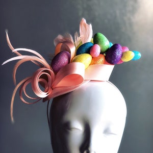 May include: A pink headband with a pink satin bow and a cluster of colourful glittery Easter eggs.