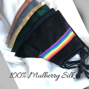 May include: A stack of six face masks made of 100% mulberry silk. The top mask is black with a rainbow stripe. The other masks are in various colors, including green, blue, and brown.