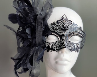May include: A black masquerade mask with intricate lace detailing and rhinestones. The mask is adorned with a black feather and lace embellishment.