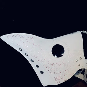 Puede incluir: M&aacute;scara de m&eacute;dico de la peste de cuero blanco con una pieza de ojo negra y detalles florales rosas. La m&aacute;scara tiene m&uacute;ltiples ojales y remaches.