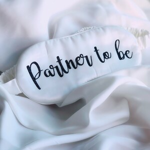 May include: White satin sleep mask with black text that reads "Partner to be".