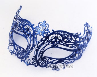 May include: A navy blue masquerade mask with an intricate, openwork design. The mask is embellished with sparkling rhinestones and features a delicate, symmetrical pattern. The text "HigginsCreek" is visible on the mask.