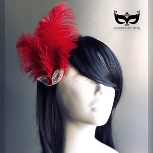 May include: A red feather hair clip with a silver and rhinestone embellishment. The clip is on a black wig.